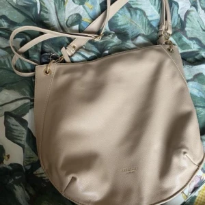 Beige axelväska Art Street london - Snygg beige axelväska från Art Shell i slätt skinnimitation. Väskan har justerbar axelrem och guldfärgade detaljer💕