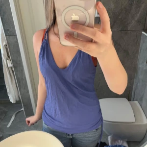 Blå linnetopp från Filippa K - Supersnygg blå linnetopp från Filippa K med twistade axelband och djup v-ringning. Toppen är ärmlös och har knyt i sidorna för en extra cool detalj. Tillverkad i mjuk viskos som känns skön mot huden. Perfekt för varma dagar och enkel att styla med jeans eller kjol.