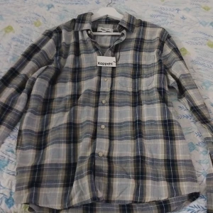 Rutig skjorta från Kappahl, blå/beige S - Snygg rutig skjorta från Kappahl i storlek S. Skjortan har klassisk krage, knäppning framtill och långa ärmar. Färgerna går i blått, beige och grått, perfekt för en chill och stilren look. Tillverkad i mjuk bomull som känns skön mot huden.