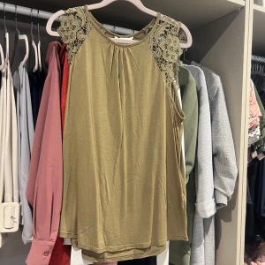 Brun linnetopp med spetsdetaljer - Snygg brun/beige linnetopp med breda axelband och spetsdetaljer i blommönster över axlarna. Ändats använd en gång!