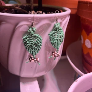 Handgjorda gröna örhängen med blommor - Unika örhängen formade som blad i ljusgrön tråd, med små pärlor och blommor i beige och brunt längst ner. Perfekta för dig som gillar boho och naturinspirerad stil. Hängande modell med metallkrok.