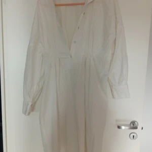 Vit lång skjortklänning från JDY - Säljer en vit lång skjortklänning från JDY med klassisk krage och knappar hela vägen framtill. Klänningen har långa ärmar med manschett och är gjord i mjuk bomull. Perfekt för dig som gillar en clean och enkel stil.