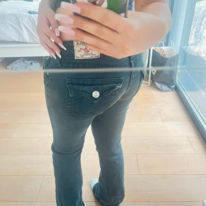 Svarta True Religion bootcut jeans - Köpt på vinted men vill ha ett andra par så säljer de.  Jeansen är vintage och är inte den ”nya modellerna” så på sista bilden kan man se att de små knapparna på sidorna är lite rostiga men inget man tänker på. Alla andra knappar är silvriga. Det är lite slitet där nere men syns inte när det är på🫶🏻 det är också lite slitningar men det är del av looken på fickorna fråga för mer bilder  Midjemått: 39 streköver