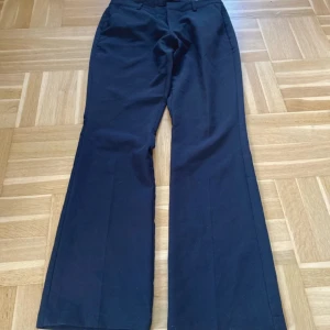 Svarta lågmidjade bootcut kostymbyxor BikBok - Snygga svarta kostymbyxor från BikBok i bootcut-modell. Byxorna har hällor för bälte, två fuskbakfickor och stängs med knapp och dragkedja. Perfekta för en clean och stilren look.