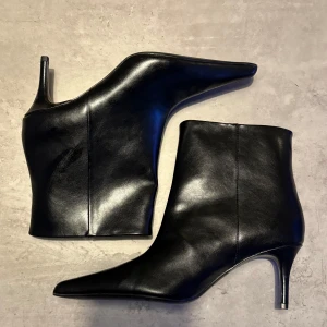 Svarta stövletter med spetsig tå - Snygga svarta stövletter från H&M i slätt skinnimitation. Modellen har spetsig tå och smal klack som ger en elegant siluett. Perfekta för dig som vill ha en stilren och trendig look med lite edge.