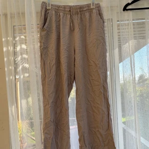 Beige linnebyxor från 157, storlek S - Luftiga och sköna beige linnebyxor från 157 med resår och snörning i midjan. Perfekta för varma dagar och chill vibes. Byxorna har raka ben och sidofickor för en avslappnad look.