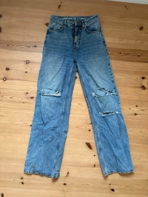 Blå raka jeans - Säljer ett par ljusblå raka jeans med hög midja och slitna detaljer över båda knäna. Storlek 27 i midja och 32 i längd