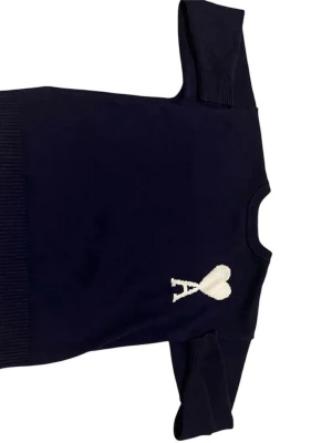 Mörkblå stickad tröja från Ami - Snygg mörkblå stickad tröja från Ami Alexandre Mattiussi med vit broderad logga i form av ett hjärta och bokstaven A på bröstet. Tröjan har rund hals, ribbade muddar och långärmad passform. Perfekt för dig som gillar stilrena detaljer.