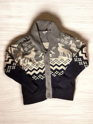 Mörkblå och grå kofta med mönster - Säljer en mysig kofta från Murina i mörkblått och grått med vinterinspirerat mönster och renar. Koftan har knappar framtill, ribbade muddar och två fickor. Perfekt för kalla dagar och snygg till jeans eller kjol.