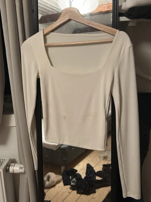 Beige långärmad topp med fyrkantig ringning - Säljer en stilren beige topp med lång ärm och fyrkantig ringning. Toppen har en enkel och clean design som passar till mycket. Materialet känns mjukt och stretchigt, vilket gör den bekväm att bära. Perfekt att styla med jeans eller kjol. Tvättas såklart innan post
