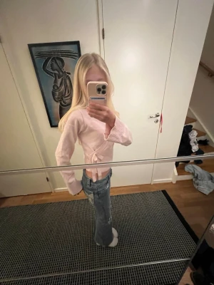 Ljusrosa omlottkofta med knyt - Supersöt ljusrosa omlottkofta med knyt i sidan och bred ribbad kant nedtill. Koftan har lång ärm och är croppad i modellen, perfekt till jeans eller kjol. Mjuk och skön, passar perfekt för vår eller höst.