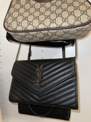 Ny Svart axelväska från YSL - Splitterny väska från YsL, oanvänd, bandet är vikt inuti väskan. Kan bli längre och kortare . Riktigt fin och populär modell. Öppen för bud! Finns i Malmö så kan hämtas/levereras så slipper du betala frakt! 