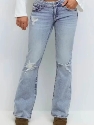 Bootcut ljusblå jeans med slitningar - Säljer ett par ljusblå bootcut jeans med slitna detaljer på lår och knän. Jeansen har låg midja, klassiska fem fickor och är tillverkade i jeansmaterial. Perfekta för dig som gillar en avslappnad och trendig look.