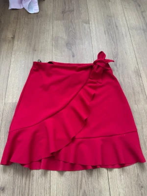 Röd volangkjol från Primark - Säljer en snygg röd kortkjol från Primark i storlek 34. Kjolen har volangdetaljer längs nederkanten och omlott-design med en rosett på sidan. ❤️pris kan diskuteras!