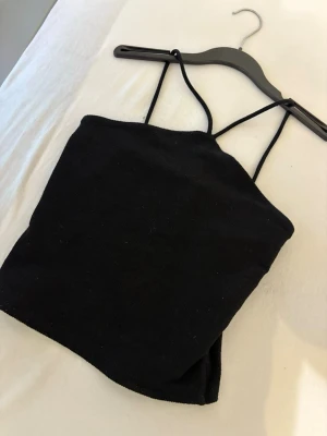 Svart stickad linnetopp - Säljer en svart stickad linnetopp med tunna axelband och enkel, rak passform. Toppen är ärmlös och har en minimalistisk look som är lätt att matcha med olika stilar. Perfekt för varma dagar eller som lager under en skjorta.