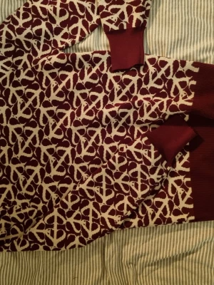 Vinröd mönstrad stickad tröja Saint Tropez - Säljer en vinröd stickad tröja från Saint Tropez i storlek S. Tröjan har ett vitt abstrakt mönster över hela och ribbade muddar vid ärmslut och nederkant. Perfekt för dig som vill ha något unikt och snyggt till hösten eller vintern.