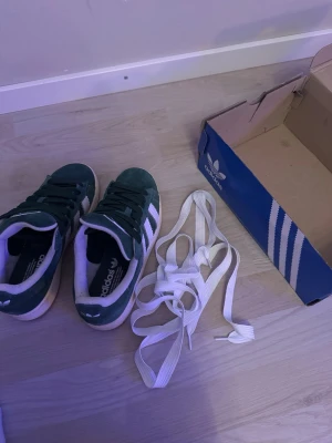 Adidas Campus gröna sneakers  - Säljer ett par gröna Adidas Campus sneakers i mocka med vita detaljer och klassiska tre ränder på sidan. Vita skosnören medföljer också. 