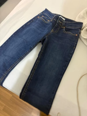 Blå jeans från Perfect Jeans, strl 32 - Säljer ett par klassiska blå jeans från Perfect Jeans i storlek 32. De har snygga kontrastsömmar, fem fickor och knappdetaljer på bakfickorna. Jeansen har normal passform och är tillverkade i slitstarkt denimtyg.