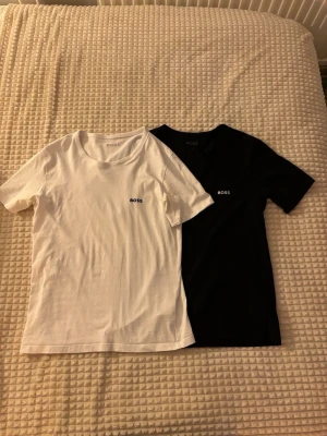 Svart och vit t-shirt från BOSS - Två stilrena t-shirts från BOSS i svart och vitt. Klassisk passform med korta ärmar och rund hals. Diskret BOSS-logga på bröstet. Perfekta basplagg till garderoben och tillverkade i mjuk bomull för skön känsla.