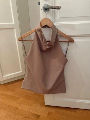 Beige halterneck topp S - Säljer en beige/ljusbrun halterneck topp från Zara i storlek S. Den är helt ny och aldrig använd. Perfekt till sommarens outfits!