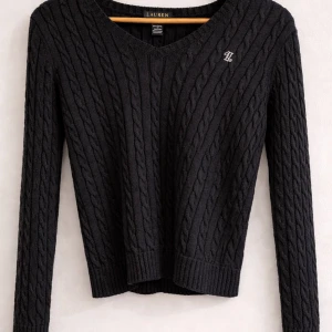 Svart kabelstickad tröja Lauren Ralph Lauren - Svart kabelstickad tröja från Lauren Ralph Lauren med v-ringning och diskret broderad logga på bröstet. Tröjan är i 100% bomull, har långa ärmar och ribbade muddar. Ordinarie pris ca 2300kr