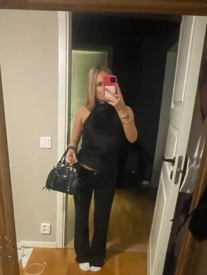 Svart satin fest topp från Zara - Säljer en svart ärmlös polotopp från Zara i glansigt satinmaterial. Toppen har hög hals med lätt drapering och knäppning i nacken. Perfekt att styla med jeans eller kjol för en snygg look. Med öppnen i rygg