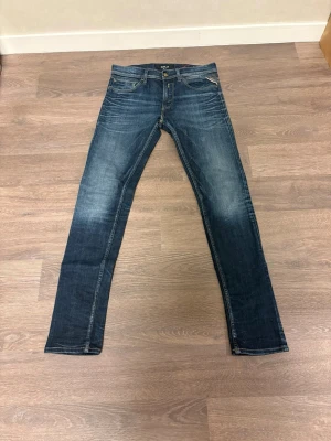 Replay jeans i mörkblå denim - Säljer ett par snygga Replay jeans i mörkblå tvätt med slitningar och klassiska fem fickor. Jeansen har raka ben och normal passform, med tydliga Replay-detaljer på fickorna och gylf med knapp. Perfekta för dig som gillar stilrena och tidlösa jeans.