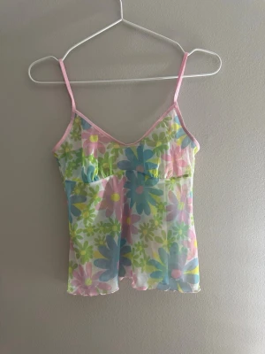 Blommig mesh linnetopp från Sloggi - Superfin mesh linnetopp från Sloggi med stora blommor i blått, rosa, grönt och gult. Topp med tunna rosa axelband och v-ringning, perfekt för sommarens alla tillfällen. Tunt och luftigt material som känns riktigt fräscht och färgglatt.