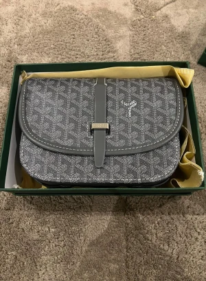 Grå mönstrad väska - Säljer en grå axelväska med ikoniskt geometriskt mönster och vita detaljer. Väskan har ett lock med spänne och snygga sömmar runt kanterna. Perfekt storlek för det viktigaste och en riktigt stilren accessoar.