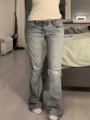 Levis ljusblå bootcut jeans - Ljusblå Levis jeans med bootcut passform och slitna detaljer vid knä och benslut. Klassisk femficksmodell med låg midja. Perfekta för dig som gillar en avslappnad och vintage look. Tillverkade i tåligt jeansmaterial❣️passar någon som är runt 150-155