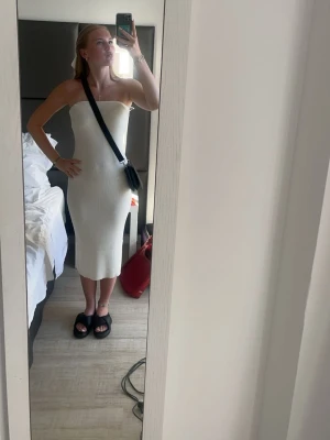 Vit axelbandslös ribbad klänning - Säljer en superfin vit axelbandslös klänning i ribbat material. Klänningen är midilång och har en tight passform som framhäver figuren. Perfekt för varma dagar och enkel att styla med accessoarer.