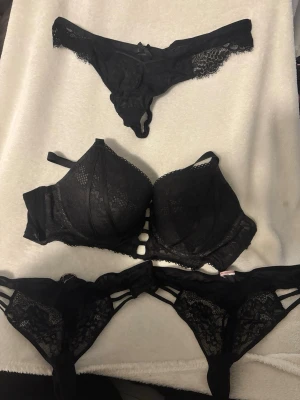Svart spets-bh från Hunkemöller - Säljer en svart bh från Hunkemöller med snygga spetsdetaljer och dekorativa band framtill. Bh:n har vadderade kupor, justerbara axelband och hakknäppning bak med coola banddetaljer. Materialet är en mix av polyamid och polyester. Och till det får du TRE matchande trosor i M från hunkemöller