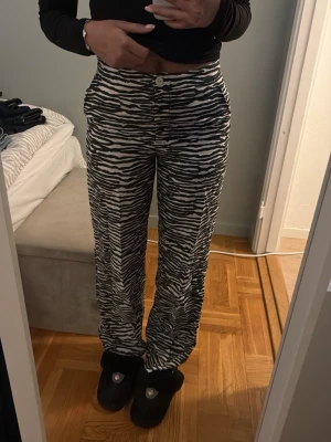 Zebramönstrade byxor från H&M - Säljer ett par svarta och vita zebramönstrade byxor från H&M i storlek 34. Byxorna har hög midja, raka ben och en loose passform. 