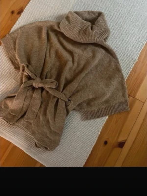 Beige polotröja med knyt från H&M - Mysig beige polotröja från H&M i stickat material. Tröjan har korta ärmar, bred polokrage och ett snyggt knytband i midjan som ger en chill och trendig look. Storleken är xs men passar både S och M. Mycket bra skick!