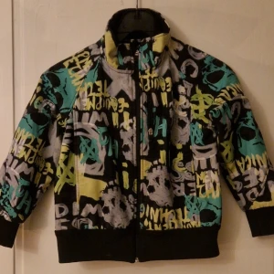 Färgglad sweatshirt/jacka - Säljer en cool sweatshirt/jacka från 180 Head Role i storlek 128 i softshellmaterial, vilket gör den tålig mot både regn och vind. Tröjan har ett färgstarkt graffitiinspirerat mönster i svart, grått, gult och turkost. Den har en ficka på bröstet och  dragkedja framtill. Perfekt för dig som gillar streetstyle! Hund finns i hemmet. Kolla in mina andra annonser för samfrakt! 