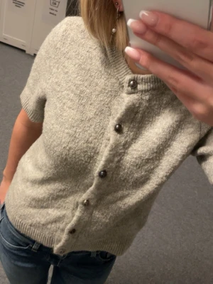 Grå kortärmad stickad kofta Gina Tricot - Kortärmad grå stickad kofta från Gina Tricot i storlek S. Ribbad vid ärmslut och nederkant. Knappar som går att ha på vilket sätt man vill. Använd men är i bra skick.