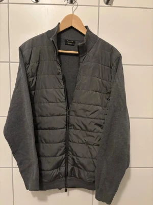 Grå quiltad jacka Massimo Dutti cardigan - Snygg grå quiltad jacka från Massimo Dutti med ribbad krage och ärmar i mjuk bomull. Framsidan är quiltad med dragkedja hela vägen och baksidan är slät. Perfekt till lager-på-lager och enkel att matcha. Inga större defekter och den är i storlek M. Hör av er vid frågor!