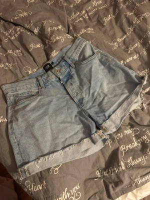 Ljusblå denimshorts från 157 - Säljer ett par ljusblå denimshorts från 157 i storlek M. Klassisk femficksmodell med hög midja och råa, fransiga benslut för en avslappnad vibe. Perfekta till sommaren och lätta att matcha med allt.