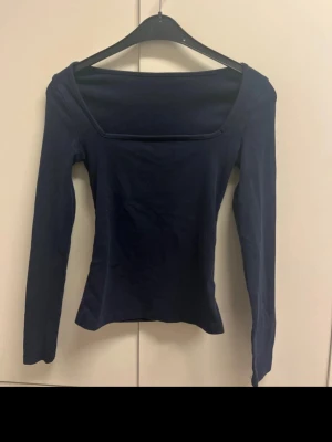 Mörkblå långärmad topp - En enkel och stilren mörkblå topp med lång ärm och fyrkantig ringning. sitter bekvämt mot kroppen. Perfekt att matcha med jeans eller kjol för en clean look.