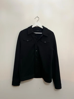 Svart overshirt från jack and jones - Säljer en stilren svart overshirt från jack and jones. Jackan har klassisk krage, tryckknappar framtill och två bröstfickor med lock. Perfekt lager-på-lager-plagg med lång ärm och enkel, clean look.