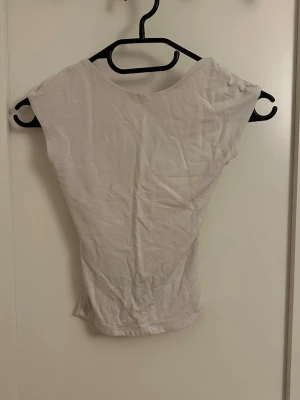 Vit ärmlös topp med öppen rygg - Snygg vit topp med öppen rygg. Perfekt för att skapa en clean och stilren look. Toppen har en enkel, rak passform och är superenkel att matcha med jeans eller kjol.
