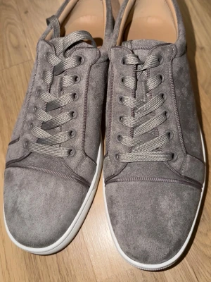 Grå mockasneakers med röd sula - Säljer ett par grå sneakers i mocka från Christian Louboutin med ikonisk röd sula. Skorna har rund tå, snörning och vita kanter runt sulan och jag skickar med dens original påse. Den är perfekta för dig som vill sticka ut, med tanke på att den är grå Christian Louboutin som har vita kant, som ger en clean men ändå unik look. Den är helt ny utan prislapp. Skriv gärna för mer detaljer.