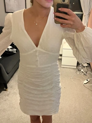 Vit studentklänning från Nelly - Supersöt vit kortklänning från Nelly, v-ringning och knappar framtill. Klänningen har långa puffärmar. Perfekt för sommaren och studenten! Storlek 36. Har endast använt en gång.