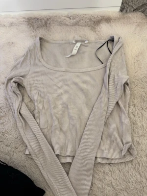 Beige ribbad långärmad topp - Säljer en beige långärmad topp med ribbad struktur och rundad halsringning. Toppen är i mjukt material och har en enkel, stilren look som passar perfekt till jeans eller kjol.