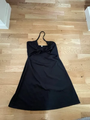 Svart halterneckklänning - Svart klänning med halterneck och knutdetalj framtill. Klänningen har en cutout på magen, mer synligt på andra bilden. Storlek 42