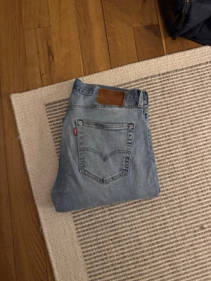 Levi's 501 ljusblå jeans straight fit - Klassiska Levi's 501 jeans i ljusblå tvätt med raka ben och normal passform. Jeansen har fem fickor, knappgylf och den ikoniska läderpatchen bak i midjan. Täcken på användning men finns fortfarande mycket kvar. 31/34