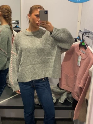 Grön stickad tröja med rosa söm - Supermysig grön stickad tröja med breda ärmar och rosa snörningsdetalj längs ärmarna. Tröjan har en loose passform och ribbad kant vid halsen. Perfekt för lager-på-lager och chill dagar. Storlek L på denna men jag har S i vanliga fall