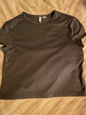 Mörk grå tränings t-shirt från Divided/H&M - En enkel svart t-shirt från Divided med rund hals och korta ärmar. Modellen är rak och har en clean look utan tryck eller detaljer. Perfekt att matcha med allt och superbekväm tack vare det släta materialet .