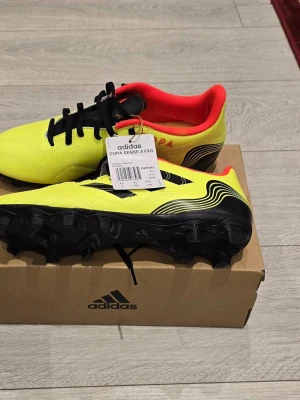 Adidas Copa Sense.4 FXG fotbollsskor - Säljer ett par Adidas Copa Sense.4 FXG fotbollsskor i neon-gult med svarta detaljer och röd insida. Skorna har klassisk snörning, svart yttersula med dobbar och är tillverkade i syntetmaterial. Perfekta för dig som vill sticka ut på planen.