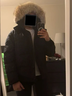 Canada goose Wyndham black label  - Säljer Canada goose wyndham med stor, fluffig luva i äkta coyote-päls i guld- och bruna toner. Jackan har hög krage, dragkedja och knappar framtill samt en klassisk, stilren look. Perfekt för kalla vinterdagar och riktigt varm. Bara Pälsen kostade mig 2460kr köpt från arcticfur   äkta coyote päls riktigt fint med metal ine i pälsen så man kan forma den utifrån preferens.
